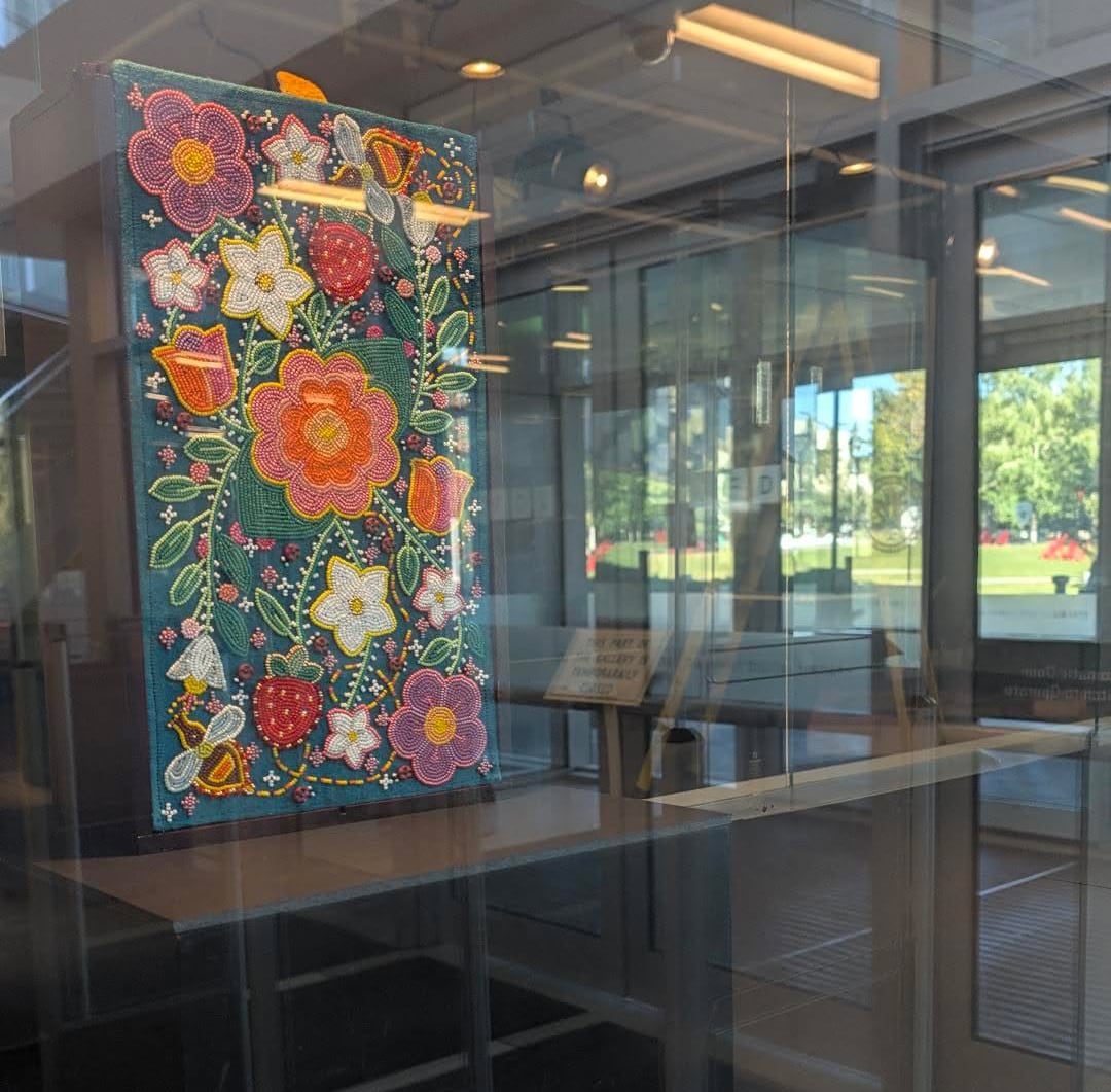 A piece of beadwork art of colourful flowers in the window of an art gallery.