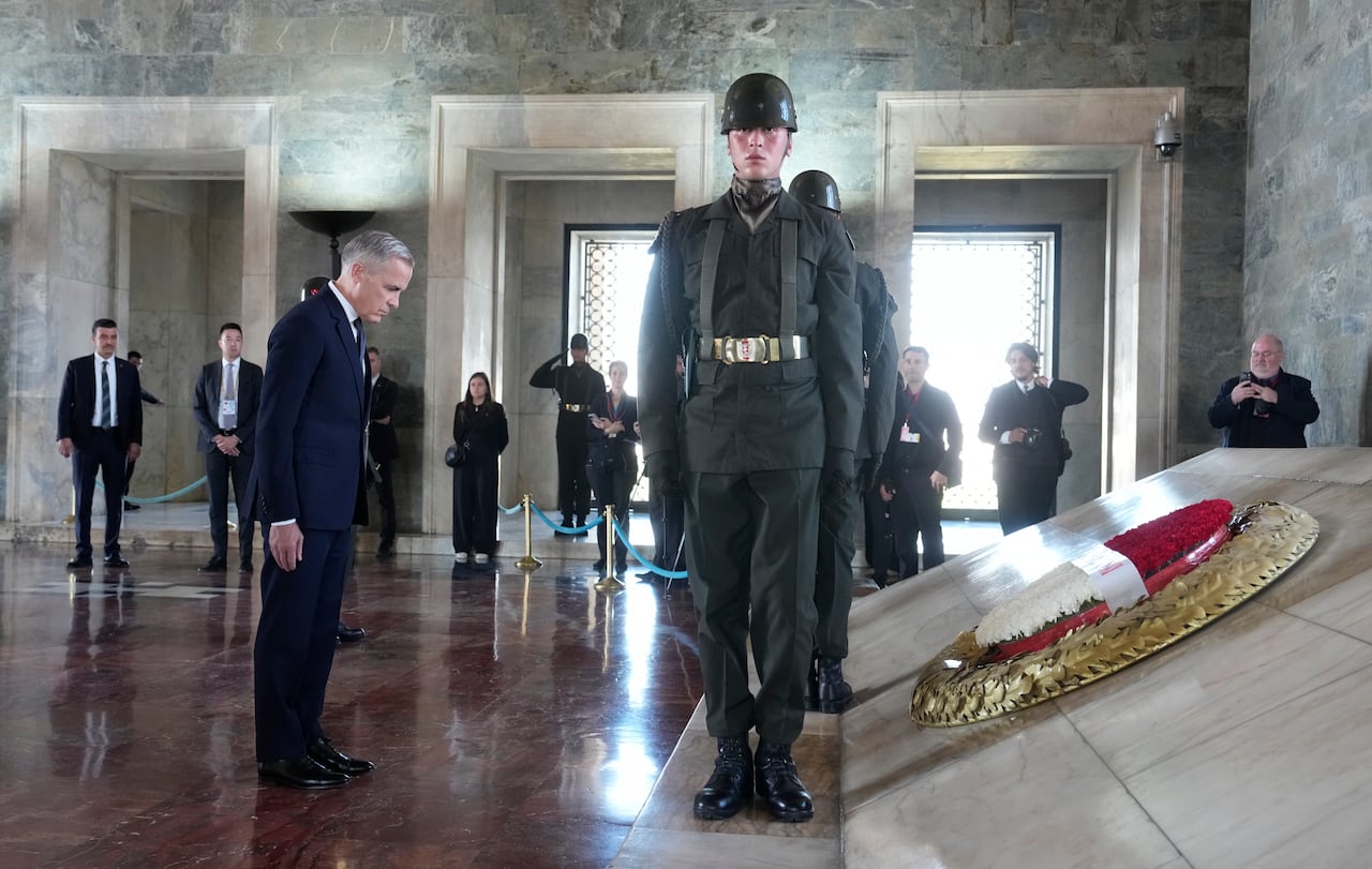 Carney stands with a bowed head as soilders stand guard.
