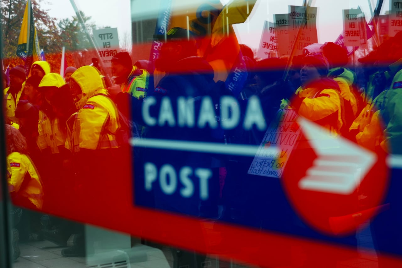 Canada Post employees and supporters rally as they are reflected in a window at Canada Post headquarters in Ottawa, Thursday, Nov. 28, 2024.