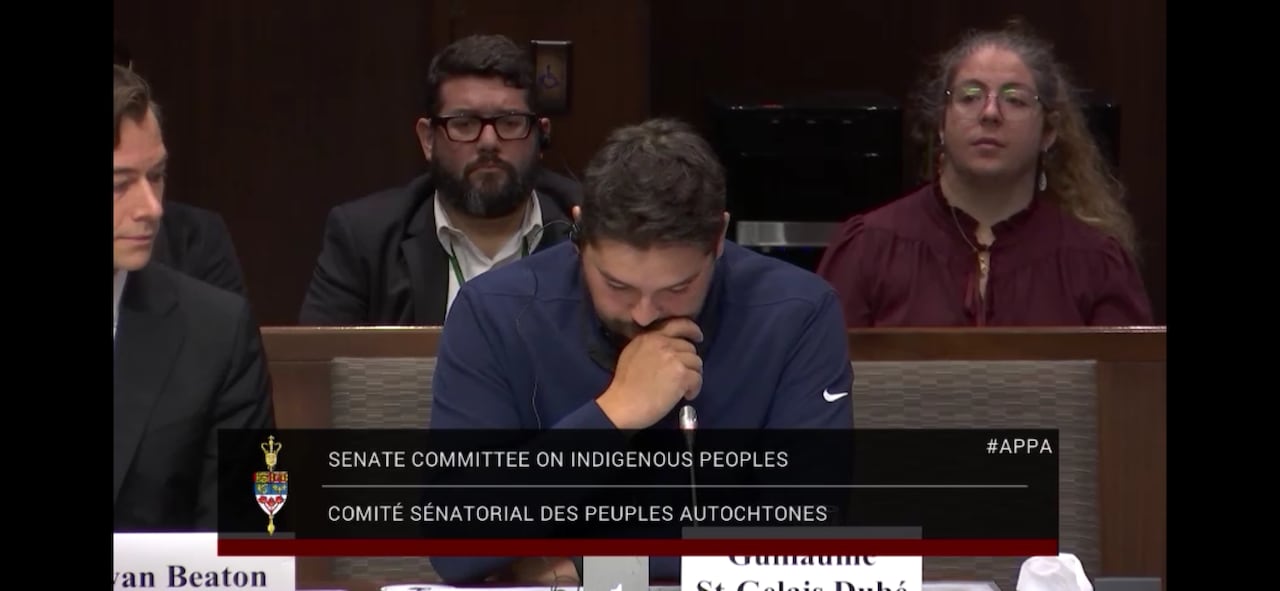 a man appears to wip tears as he testifies in a hearing room