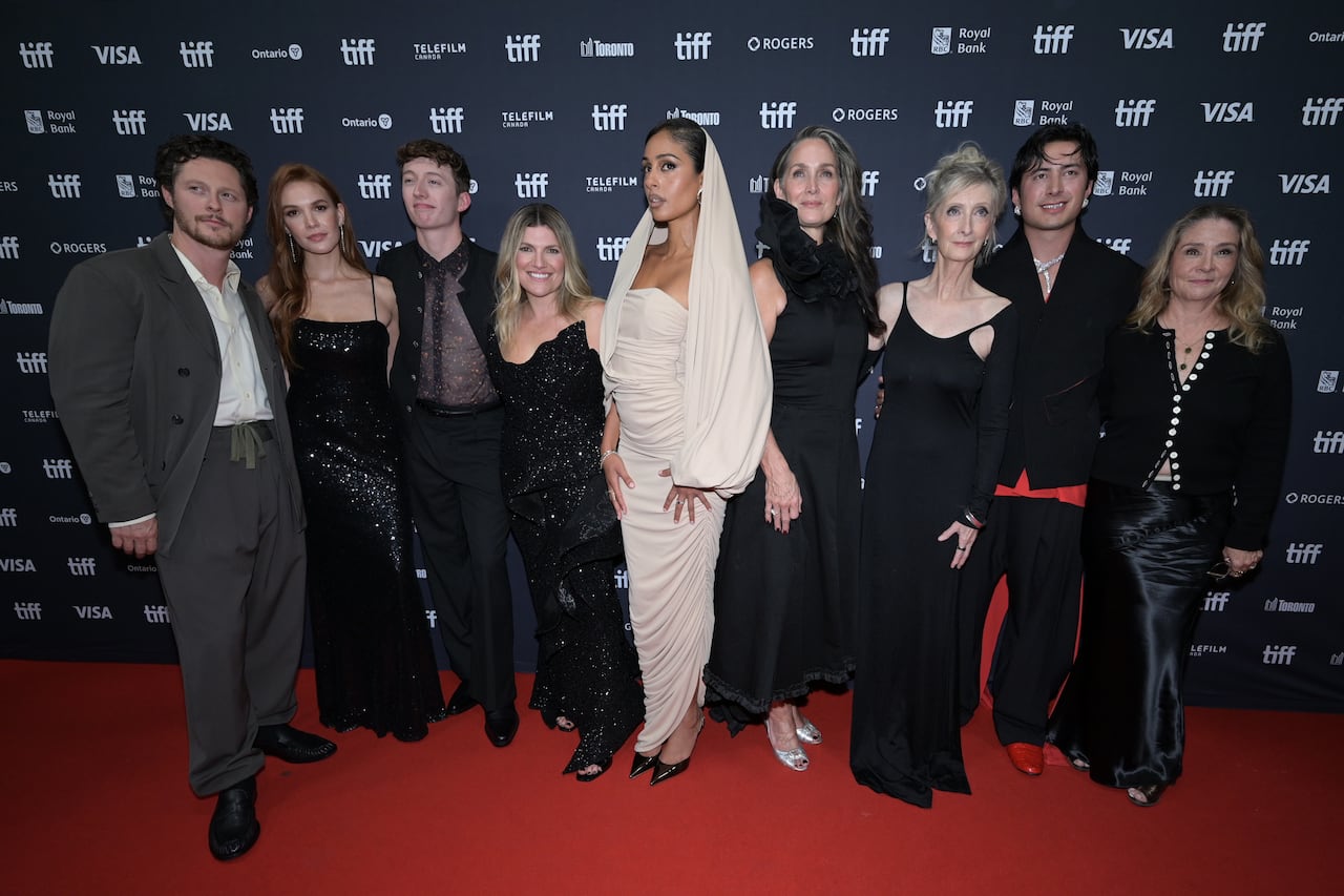 Nine people standing on on a red carpet in front of a branded wall.