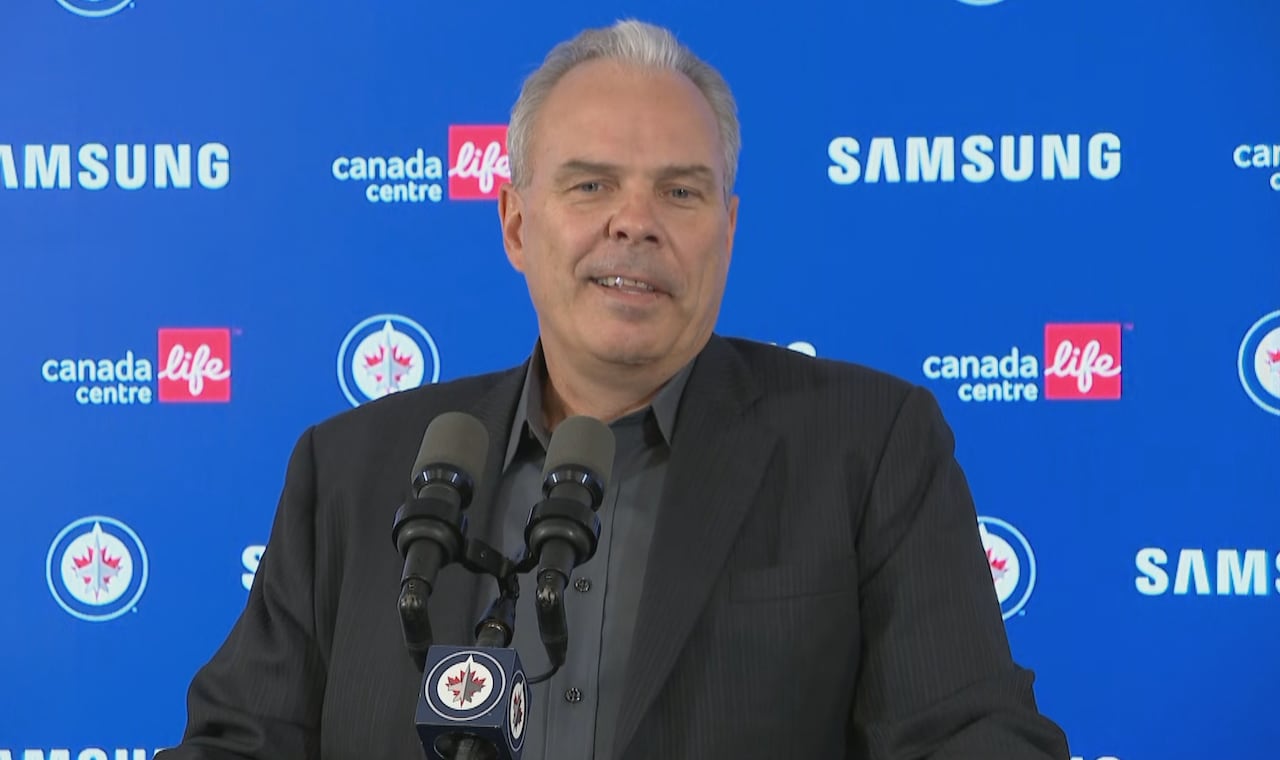 A man with grey hair stands at a podium. Behind him is a blue backdrop.