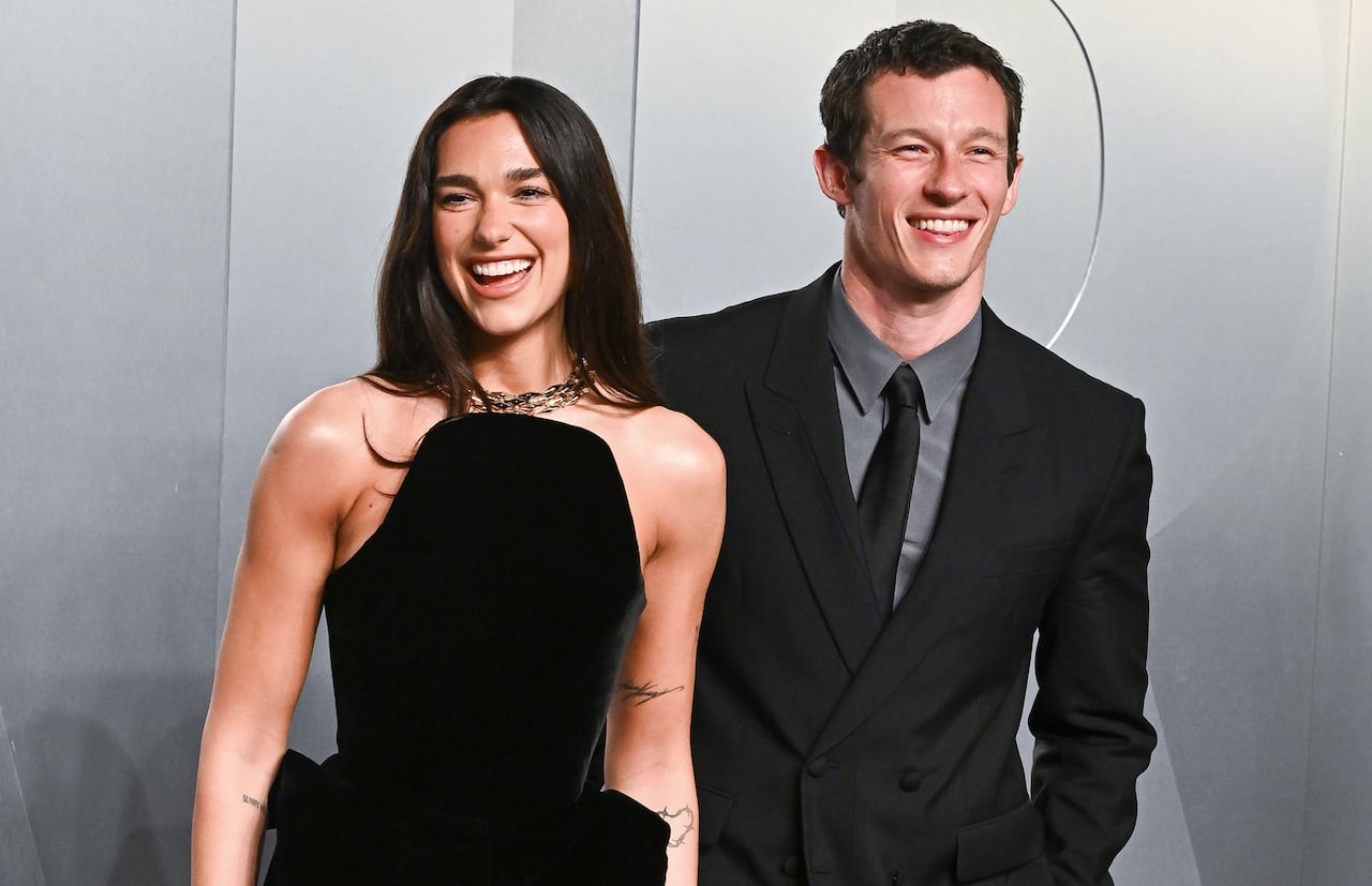 A woman in a black dress and a man in a black suit pose together, with big smiles.
