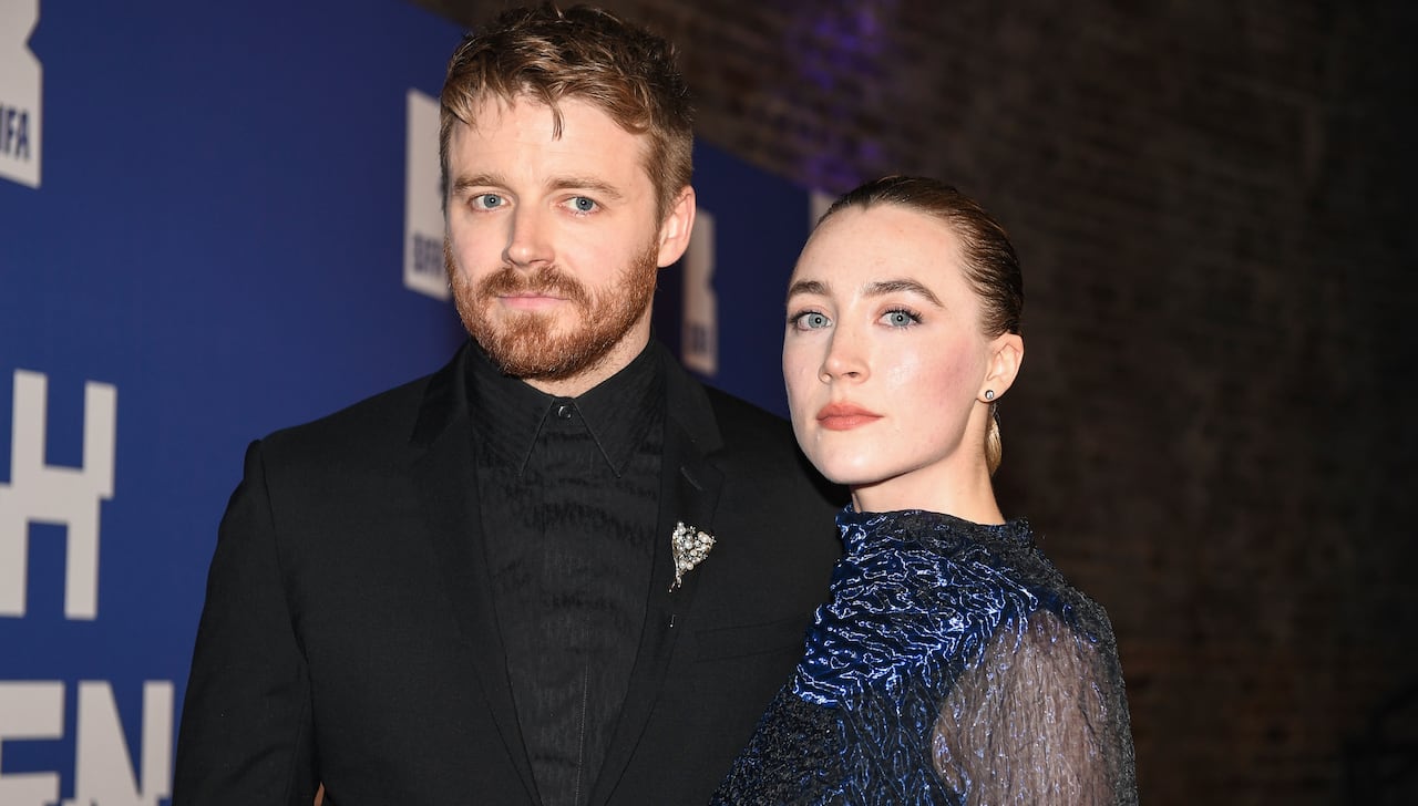 A bearded man in a suit and a woman in a fancy blue dress pose for a photo.