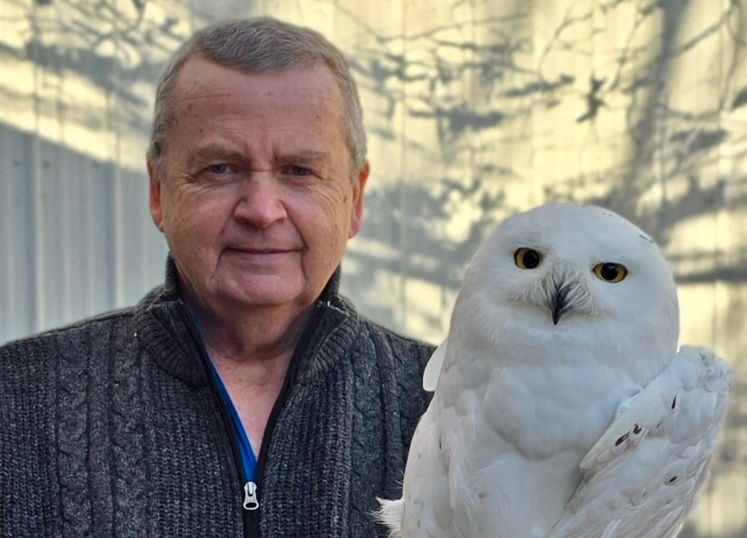 A man poses for a photo with a snowy owl.