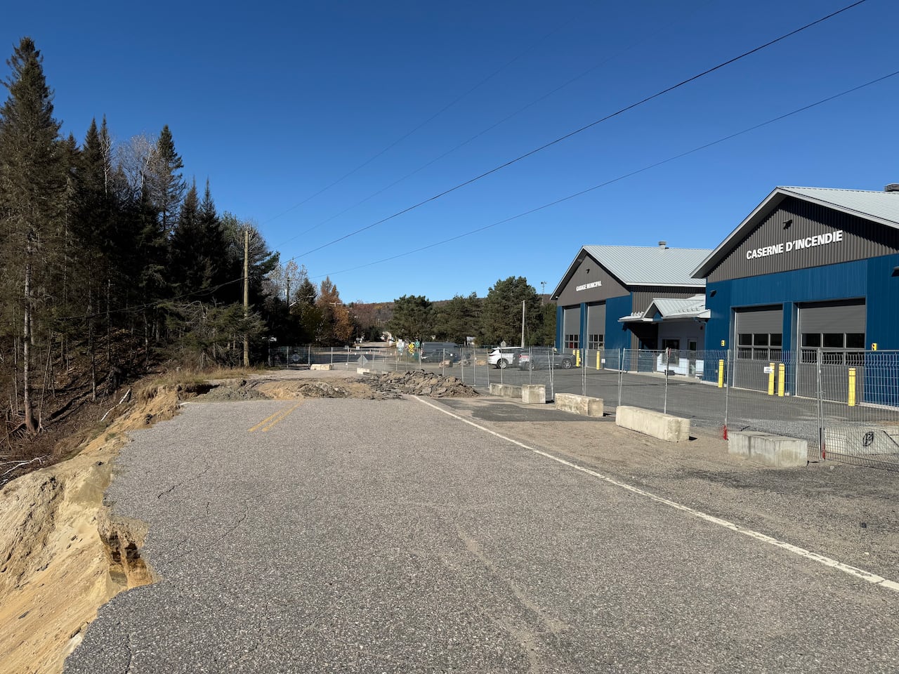 Blue buildings with white lettering that says CASERNE D'INCENDIE face a crumbing roadway that drops off into a deep trench.