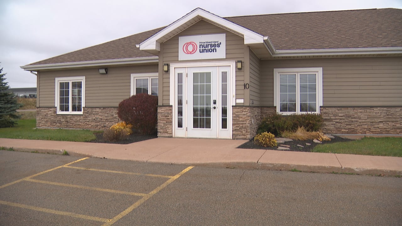 A brown building with a white door is shown from a parking lot.