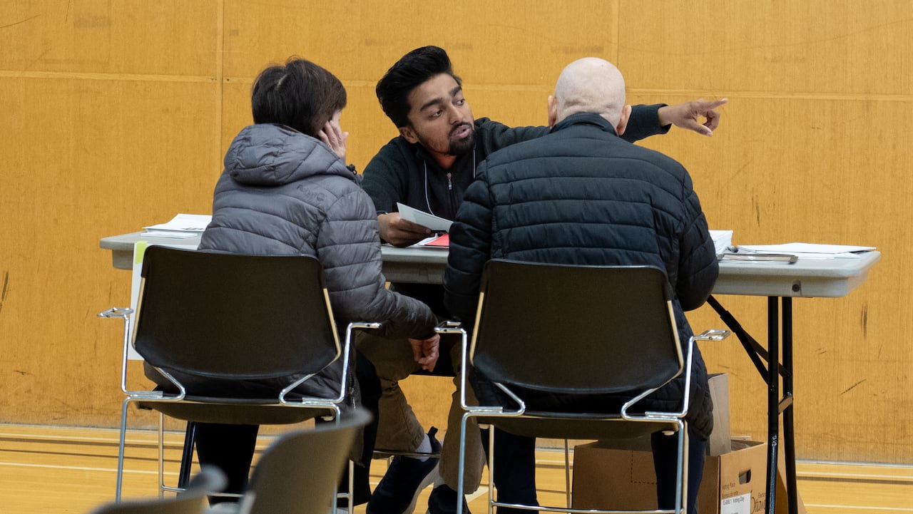 A poll worker points two people toward voting in a gym.