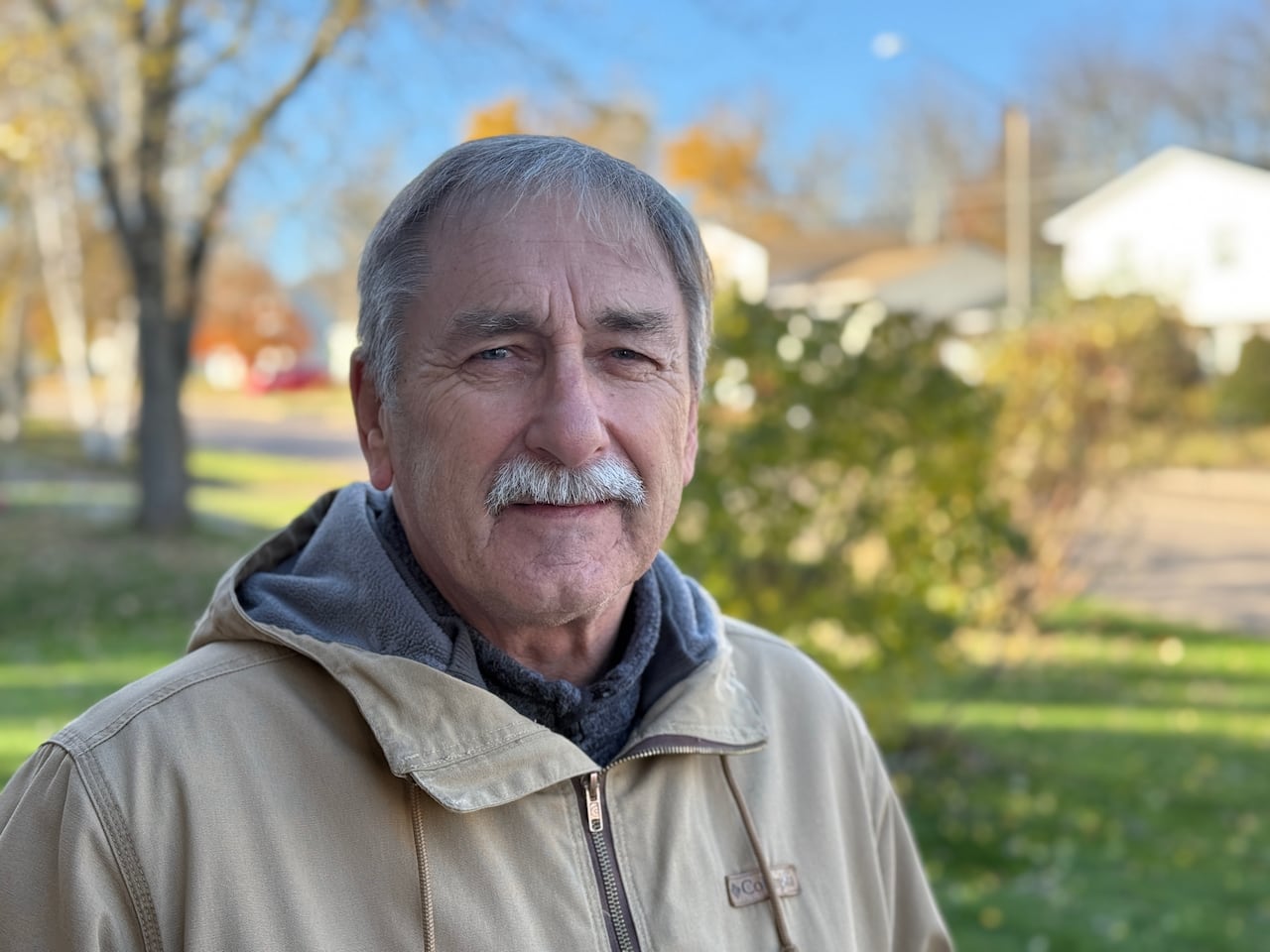 A man in a light brown coat standing outside.