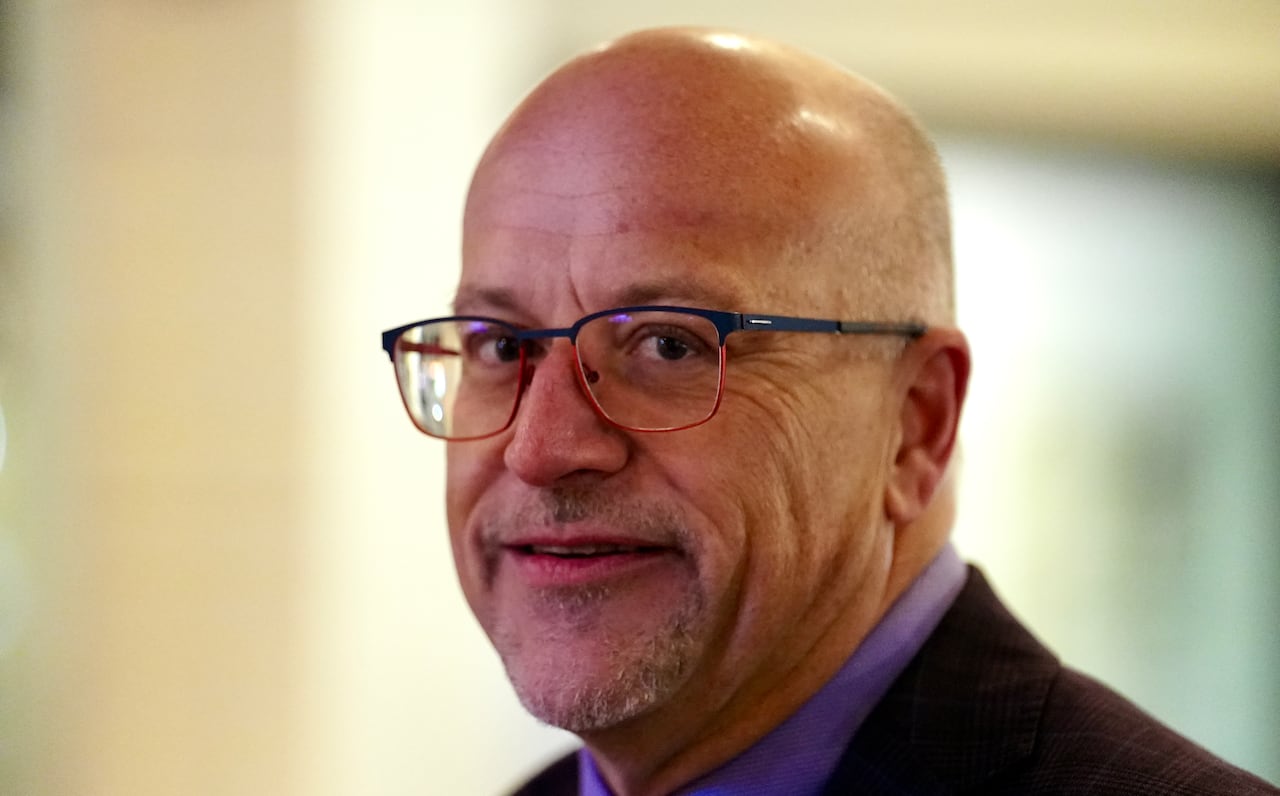 A bald man with glass looks into the camera.