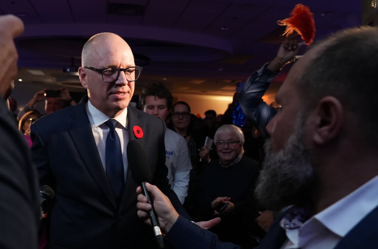 Man with black glasses wearing blue suit smiles during an interview