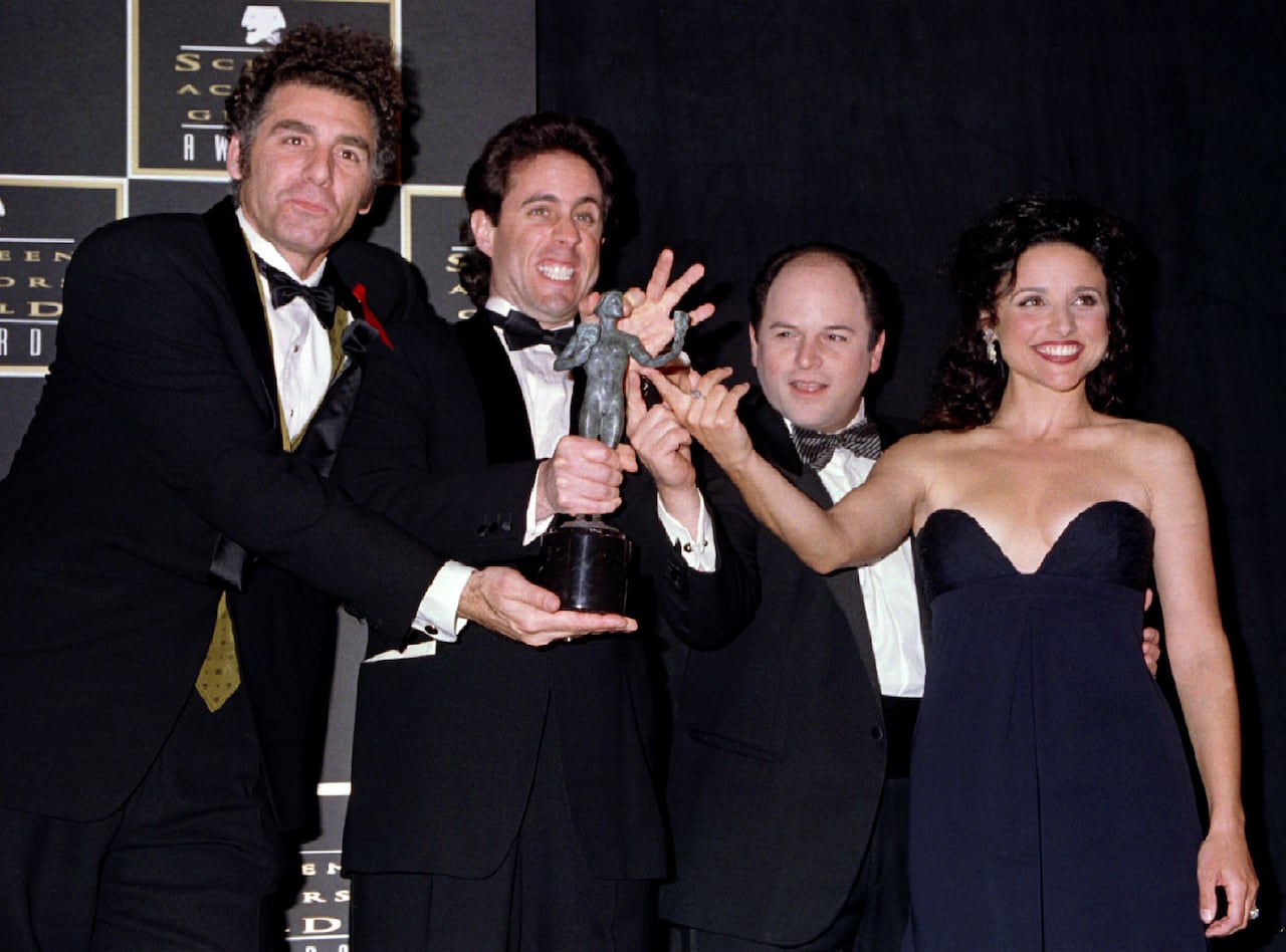Four people dressed in formal wear hold an award statue.