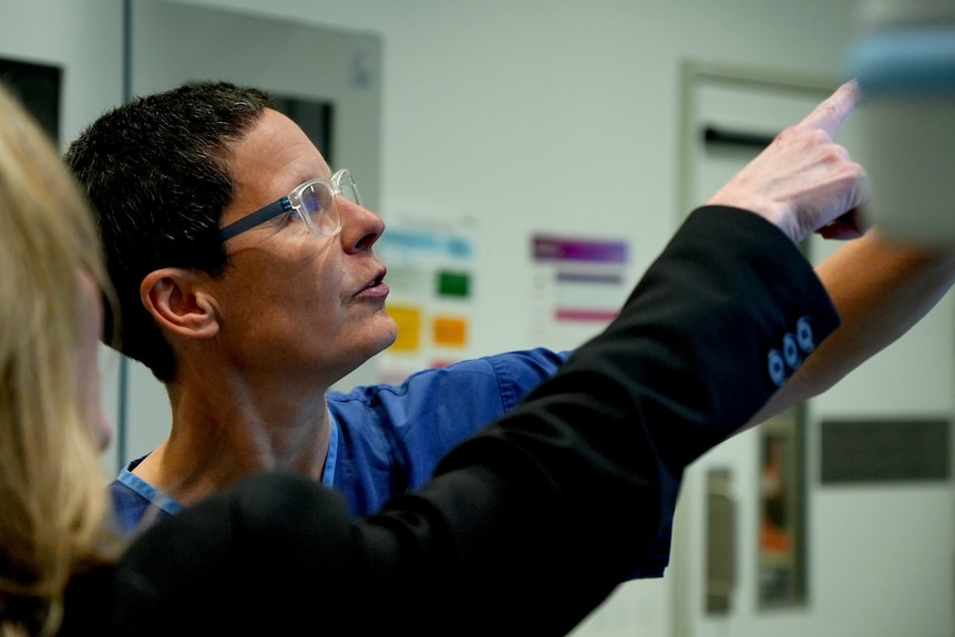 Dr Gemma Figtree in blue scrubs, short brown hair, clear glasses, pointing at a screen next to a blonde woman.