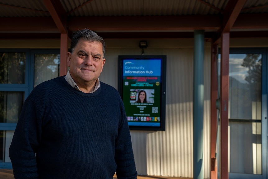 Man in a blue jumper stands in front of a building with a sign saying Shoalhaven Community Information Hub