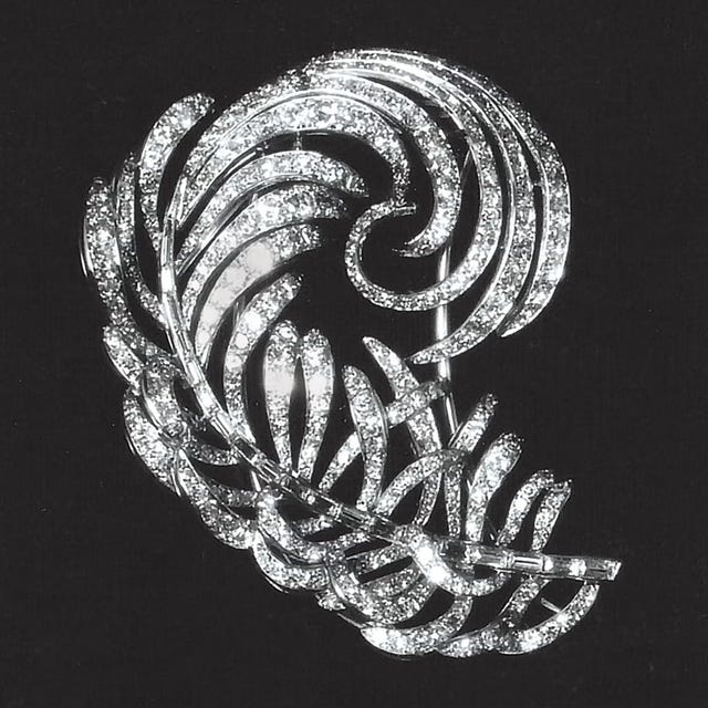 Detailed silver brooch with a swirling leaf design, encrusted with sparkling gemstones on a black background.