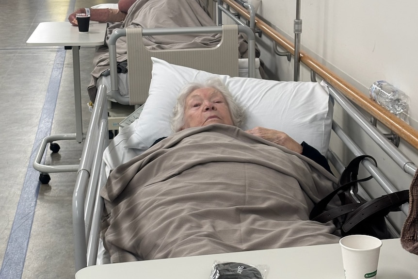 A elderly person lies in a bed at a hospital corridor.