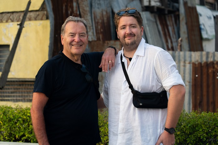 580249,TITLE:Celebrity Race Across the World Series 4 Jeff Stelling and Matt stood next to each other smiling ahead. Jeff is resting his arm on Matt's shoulder.