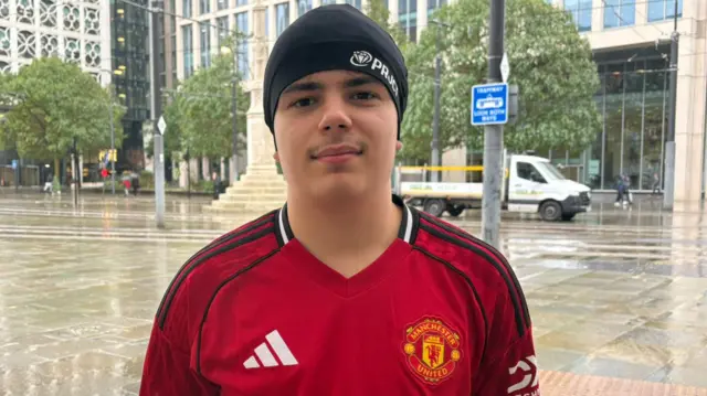Rafael Millin Fialho is in Manchester city centre wearing a red Manchester United top and a black beanie hat.