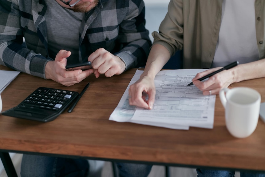 A couple seated at a table going over financial statements with a pen in hand and calculator nearby