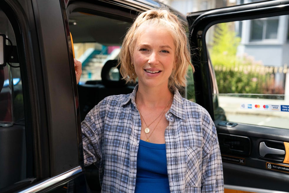 EastEnders, Nancy Carter in 2026 eastenders, maddy hill as nancy carter in 2026, wearing an open blue checkered shirt, standing in front of an open taxi door