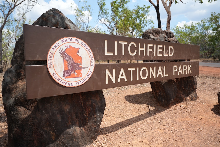 A wooden sign attached to rocks on red dirt features a Parks and Wildlife logo alongside the words: LITCHFIELD NATIONAL PARK
