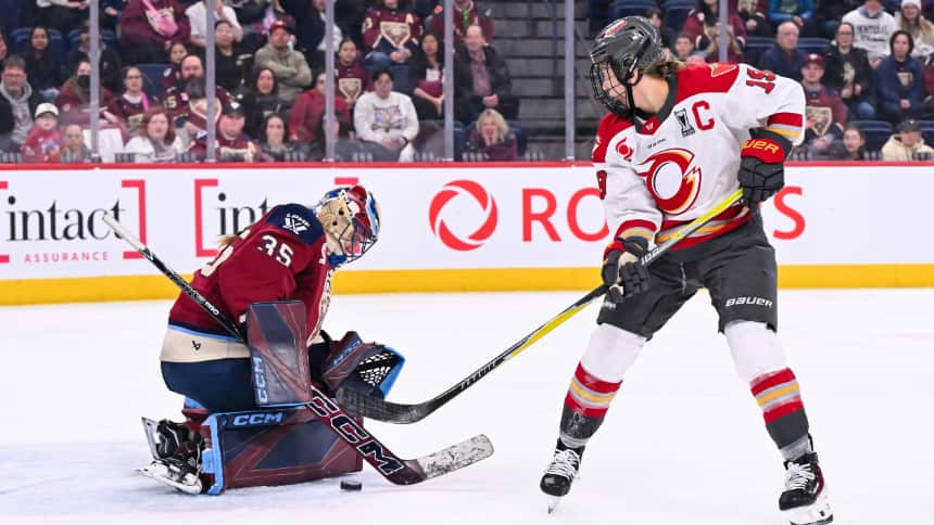 Two women hockey players in game. One wears a red jersey, left, the other wears a white jersey