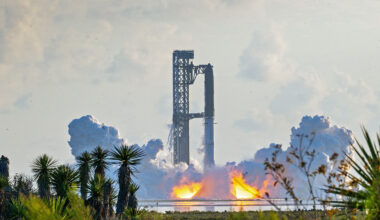 A large rocket stands on a launchpad as flames and thick clouds of smoke rise from its base.