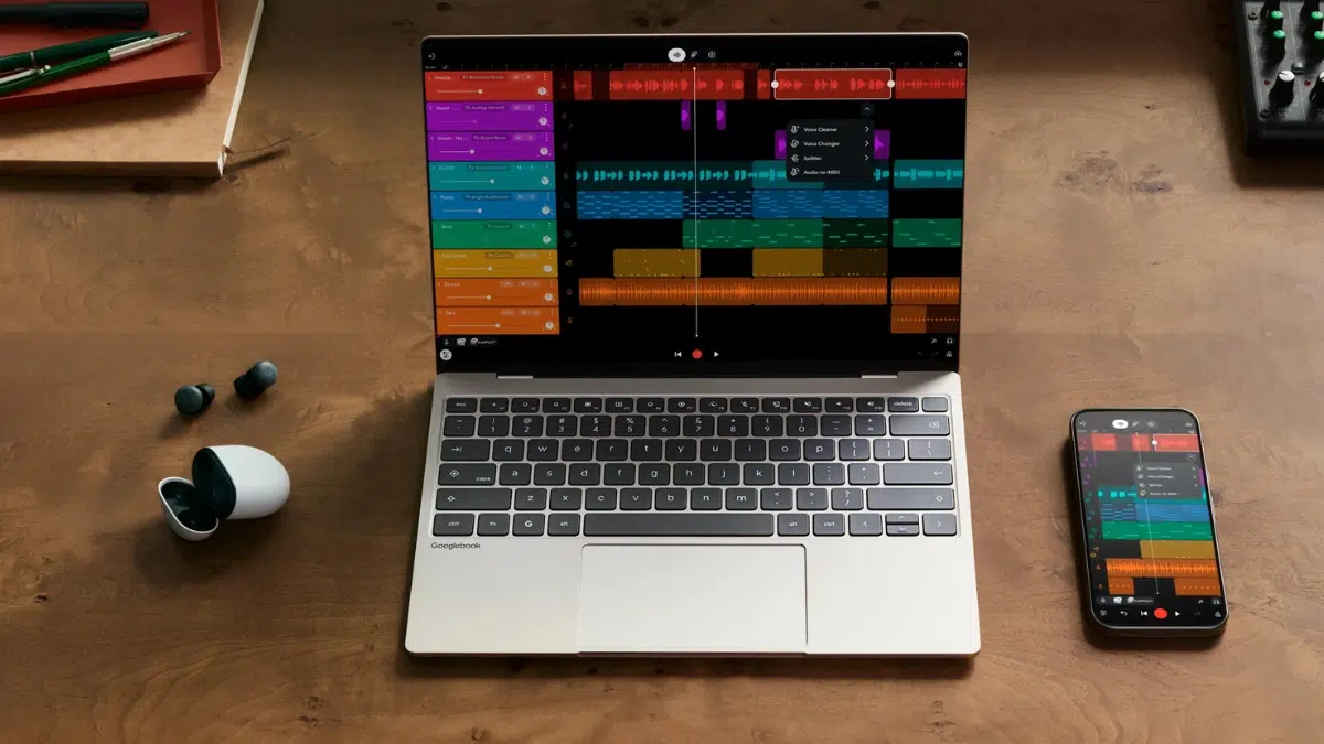 Googlebook laptop running a multitrack music editor on a wooden desk, beside a phone and earbuds