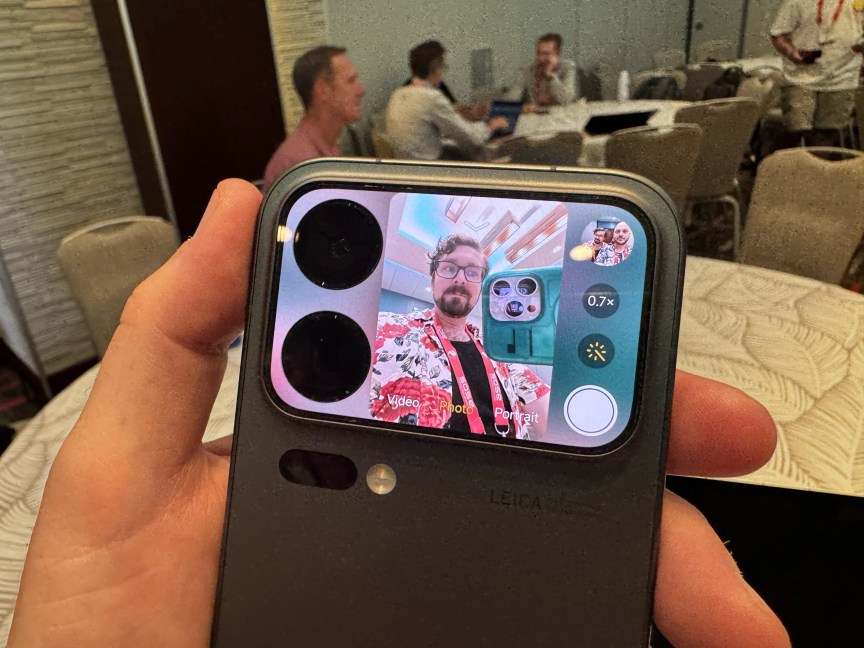 A rear phone screen next to cameras showing a preview of what they're capturing -- in this case, a man's face.