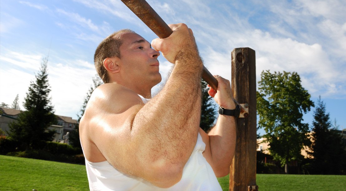 Fit man working out his biceps and arms outside with a chin up exercise