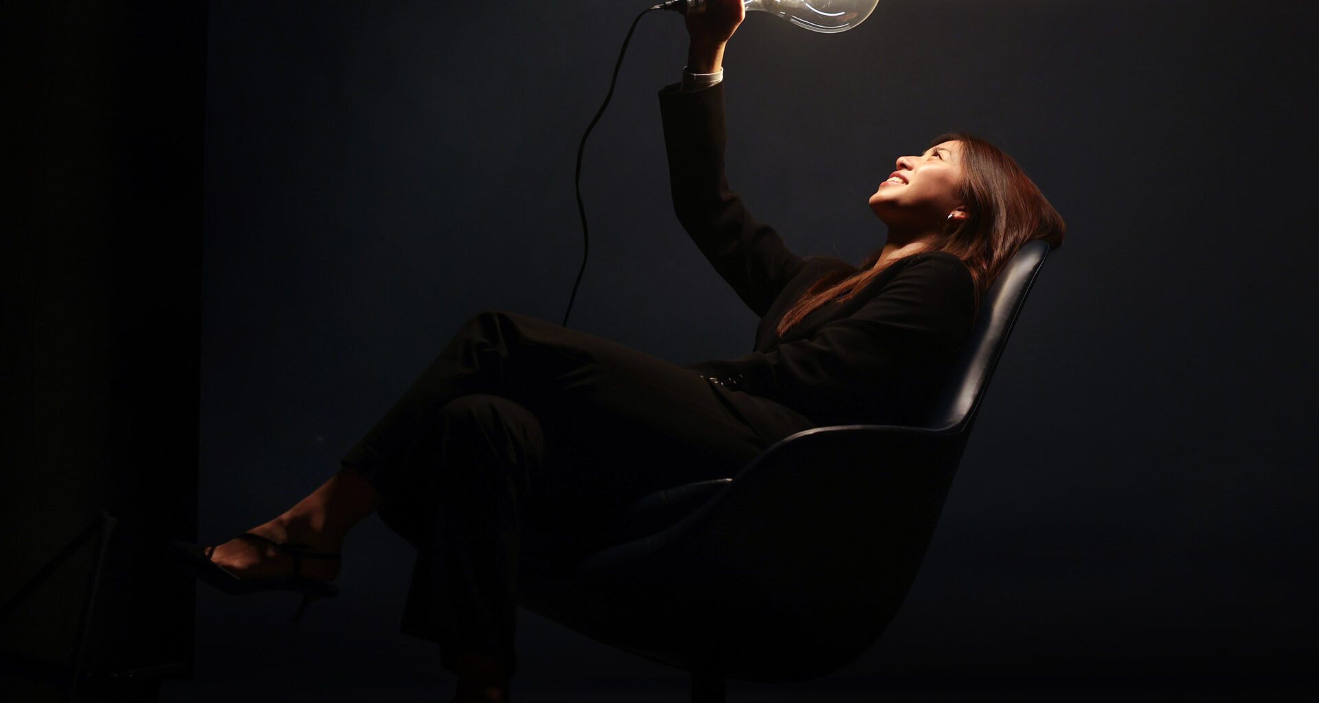 Tina Yao in black suit holding a glowing light bulb