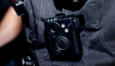 Close-up of a police body-worn camera clipped to the chest of a dark uniform shirt.
