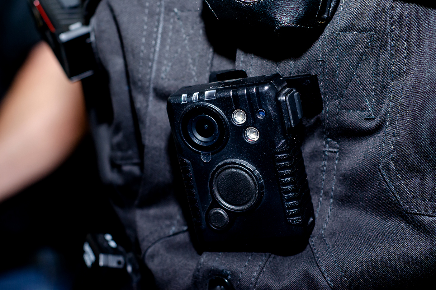 Close-up of a police body-worn camera clipped to the chest of a dark uniform shirt.