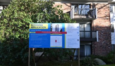 A redevelopment sign in front of a brick apartment building.