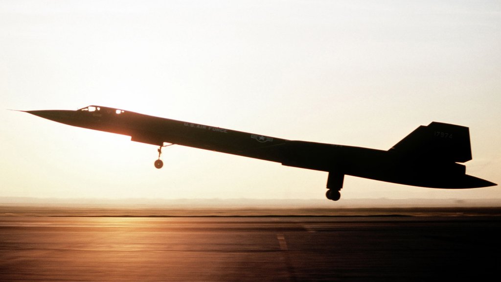 A left side view of an SR-71 aircraft from the 9th Strategic Reconnaissance Wing landing. The aircraft is silhouetted against the sunset.