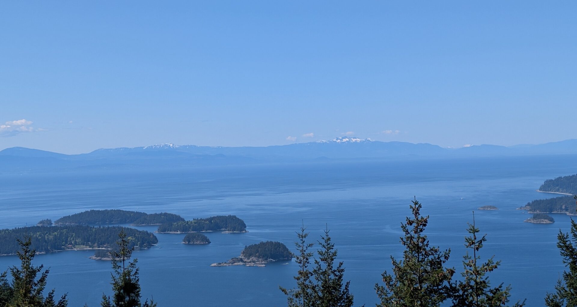 A panoramic view of islands and ocean under a clear blue sky with distant snow-capped mountains.