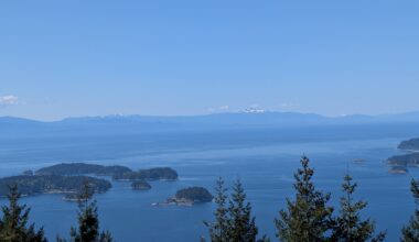A panoramic view of islands and ocean under a clear blue sky with distant snow-capped mountains.
