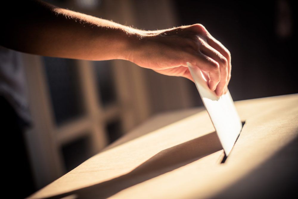 A person places a ballot into a box in a dimly lit room.