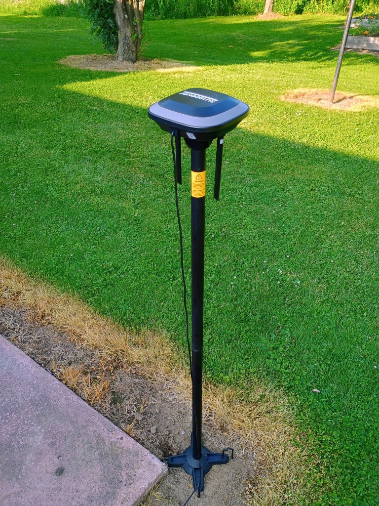 A tall black antenna stands at the corner of a patio and next to a green lawn.