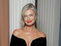 Model Paulina Porizkova wears a black long-sleeve, off-the-shoulder gown. Her gray hair is pulled back and she's wearing red lipstick.