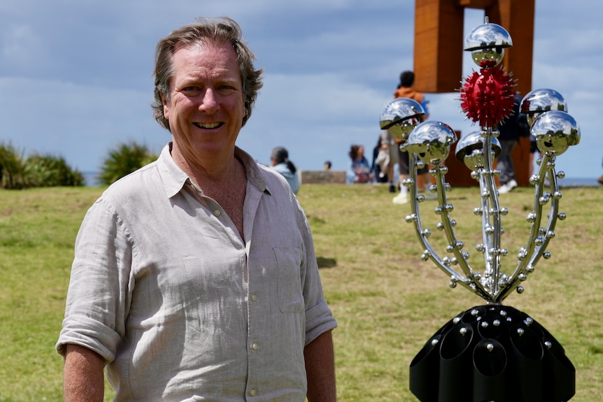 Mr Handley with short wavy brown hair smiles next to five metal reflective balls surrounding a spiky red ball.