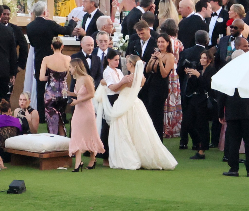 Jennifer Meyer, in a white wedding gown, hugs Courteney Cox at her wedding reception, surrounded by guests.