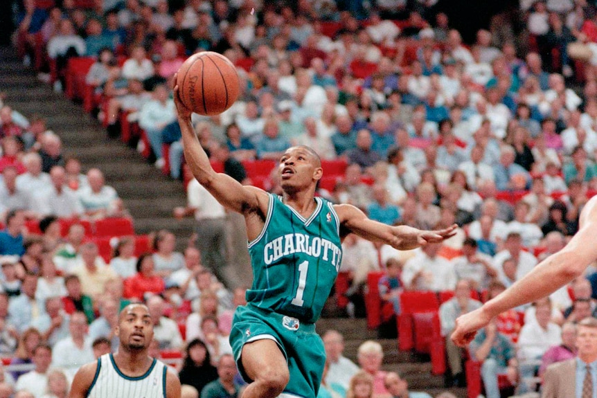 Basketballer jumps in the air, heading towards the hoop with ball in one hand