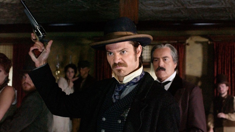 Timothy Olyphant as Seth Bullock, raising a pistol in the air in Deadwood.