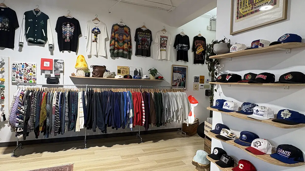Vintage hats displayed on shelves, with T-shirts and sweaters arranged on clothing racks inside The Jungle, an Ottawa vintage store.