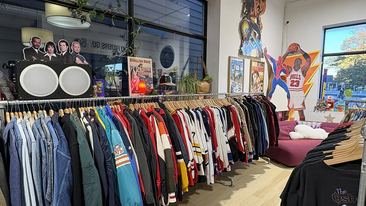 Racks of vintage jackets, sports jerseys and shirts inside The Jungle in Ottawa, with colourful posters, sports cutouts and a pink couch in the background.
