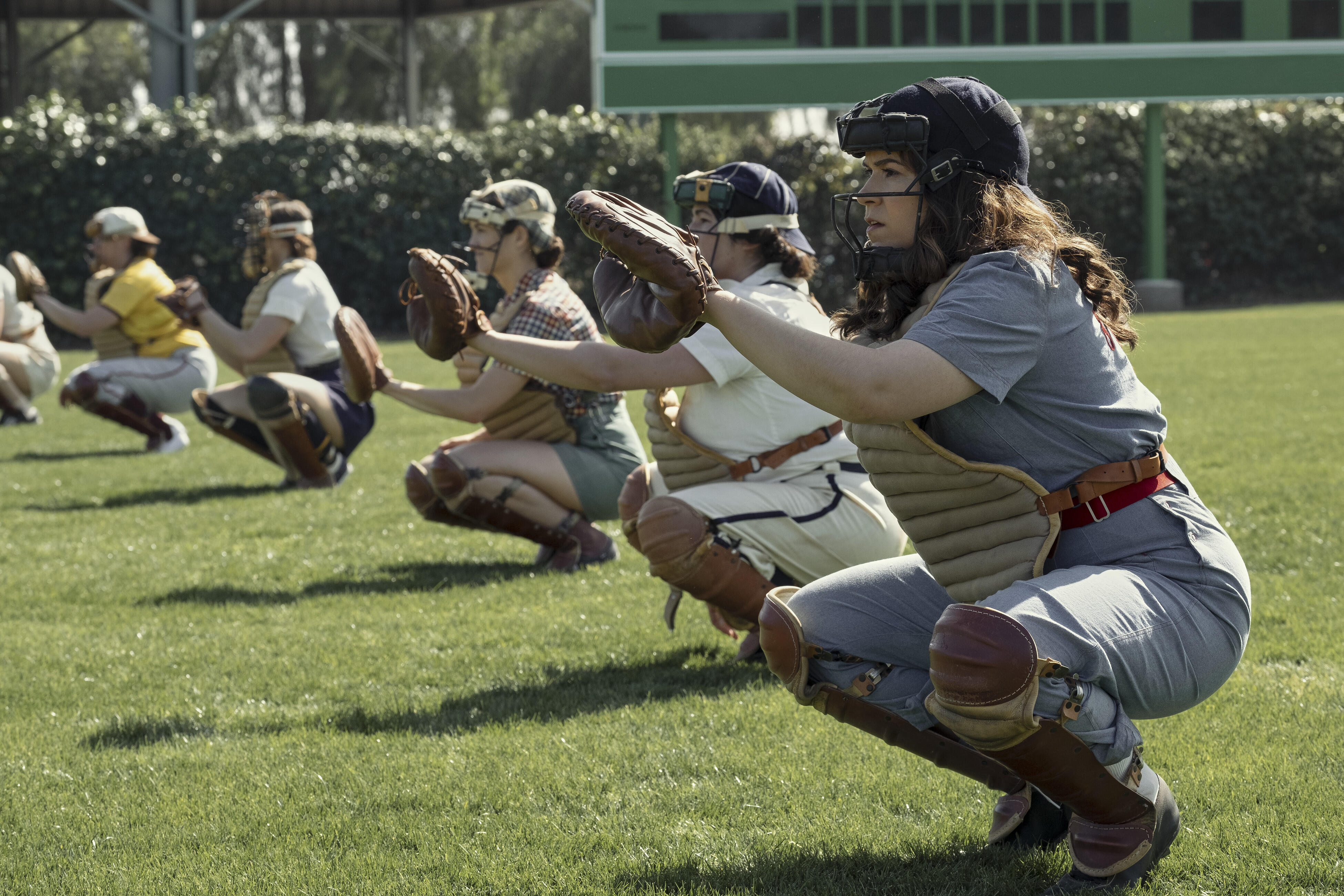 The Rockford Peaches in a line, all squatting and raising their mitts to catch a ball.