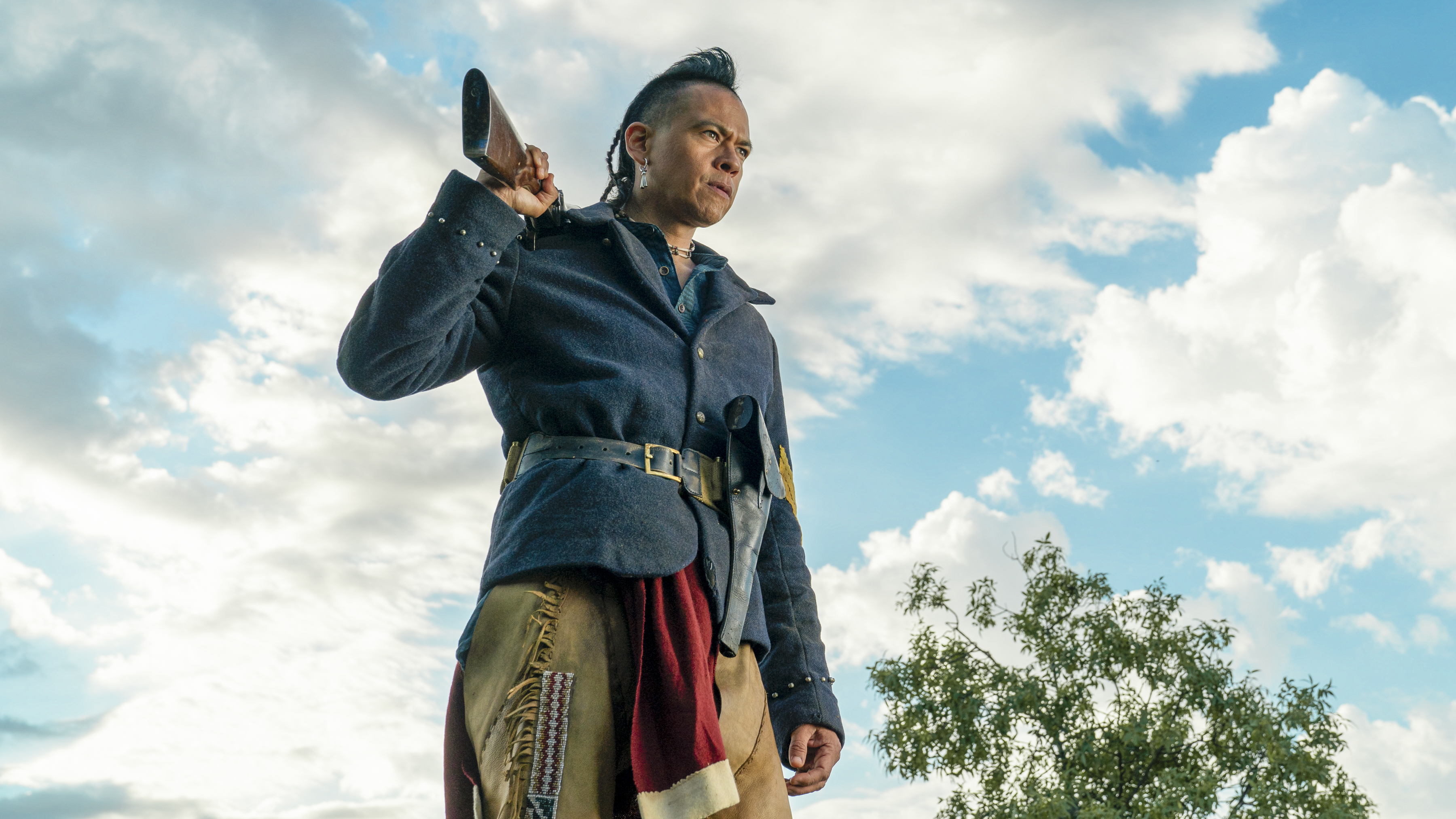 Chaske Spencer as Eli, wearing a sergeant's uniform, standing against a blue sky backdrop
