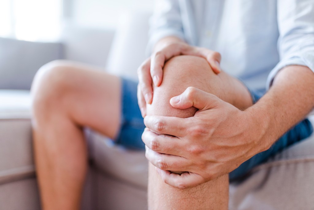 A man holding his painful knee while sitting on a sofa.