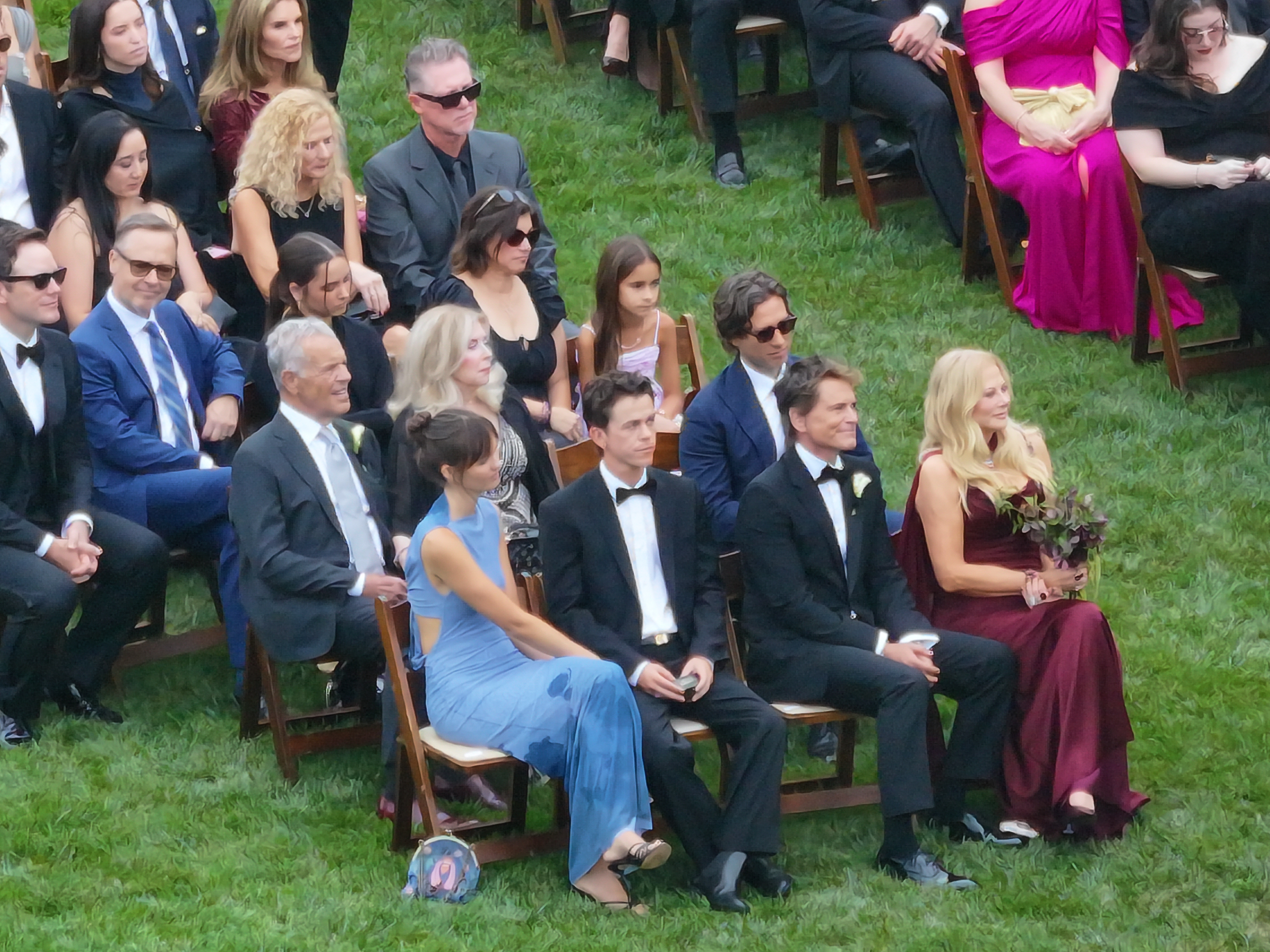 A high-angle view shows guests seated in chairs on the grass at an outdoor wedding ceremony, featuring attendees like Rob Lowe, Gwyneth Paltrow, Cameron Diaz, Katy Perry, Chris Pratt, Katherine Schwarzenegger, Maria Shriver, Zoe Saldaña, Adam Levine, and Behati Prinsloo.